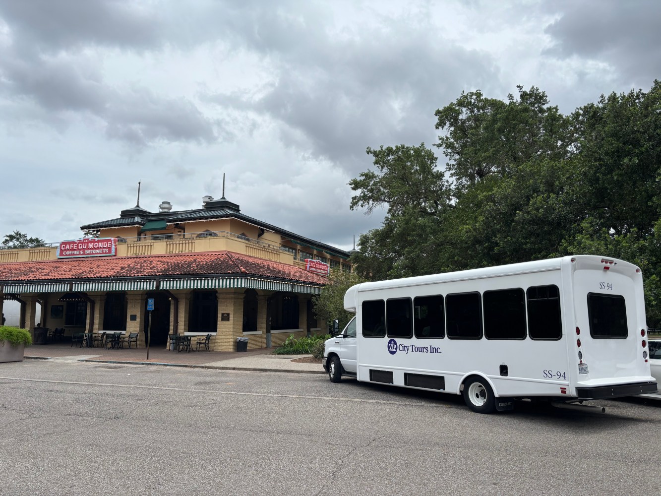 White tour bus parked in front of a cafe under a cloudy sky.