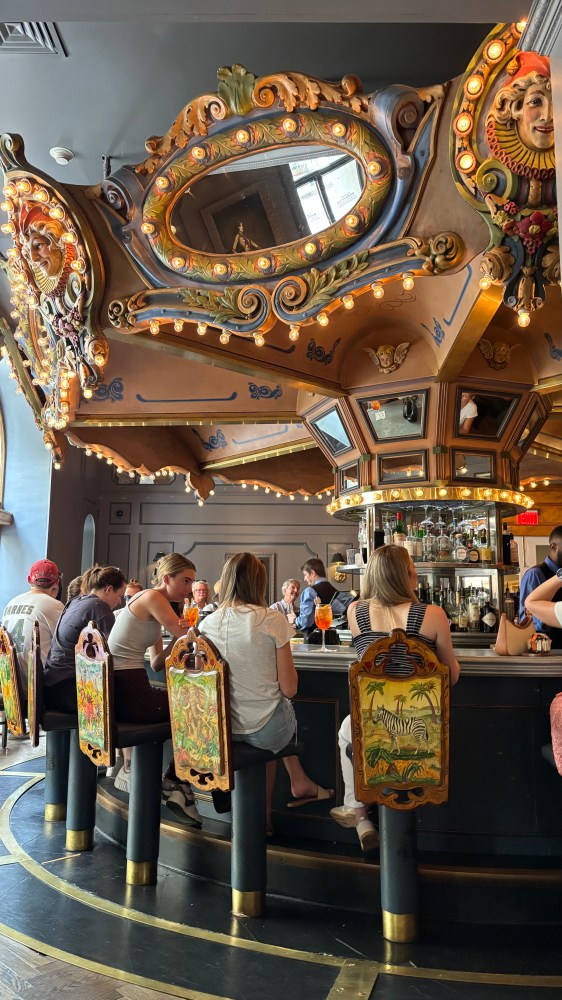 People seated at a carousel-themed bar with ornate decorations.