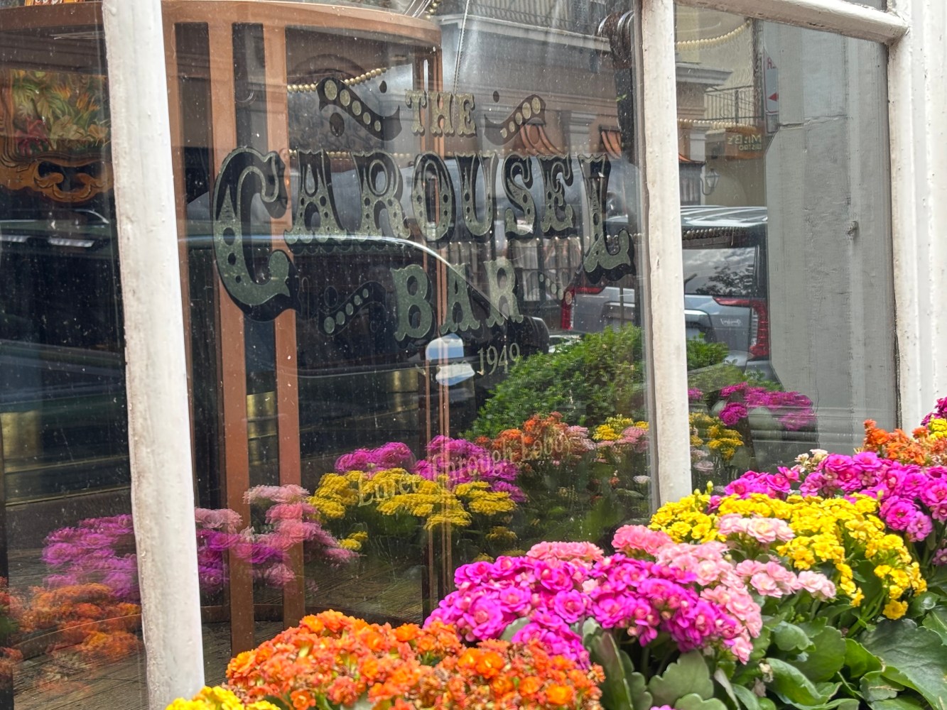 Colorful flowers reflected in a window with text 'The Carousel Bar'.