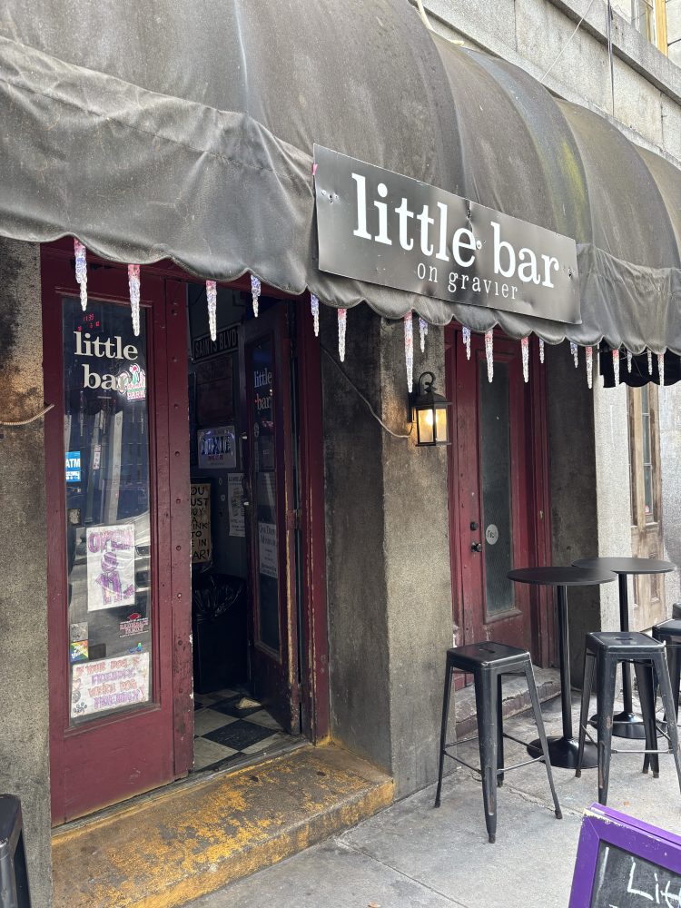 Entrance to a bar under an awning with outdoor high tables and chairs.