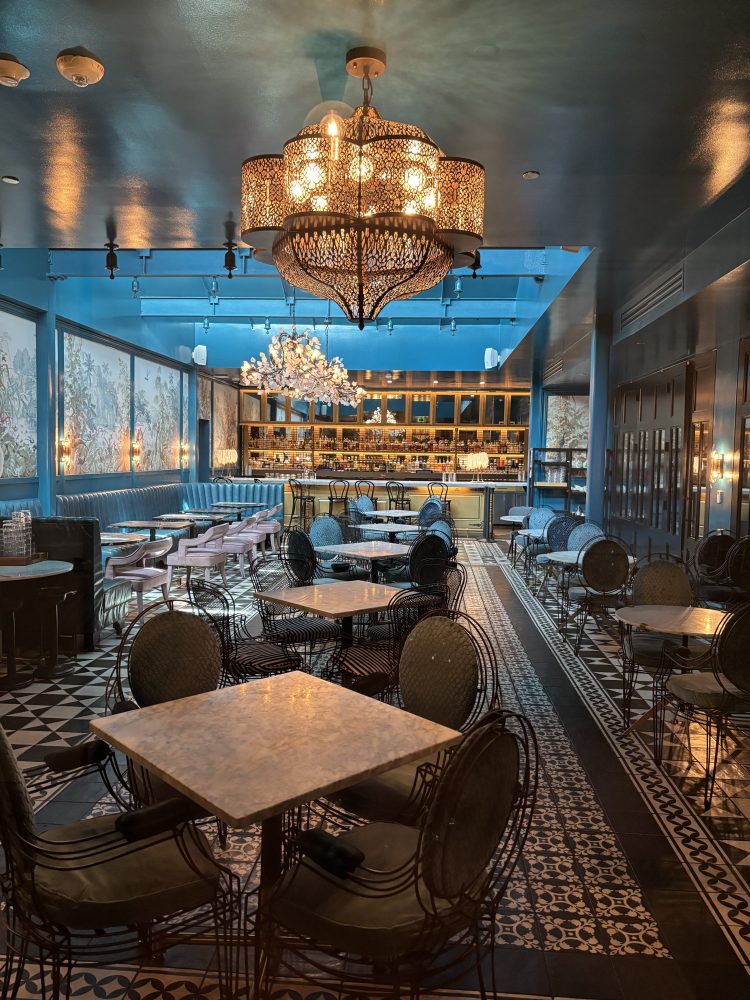 Chic, dimly-lit cafe with chandeliers, patterned floor tiles, and modern furniture.