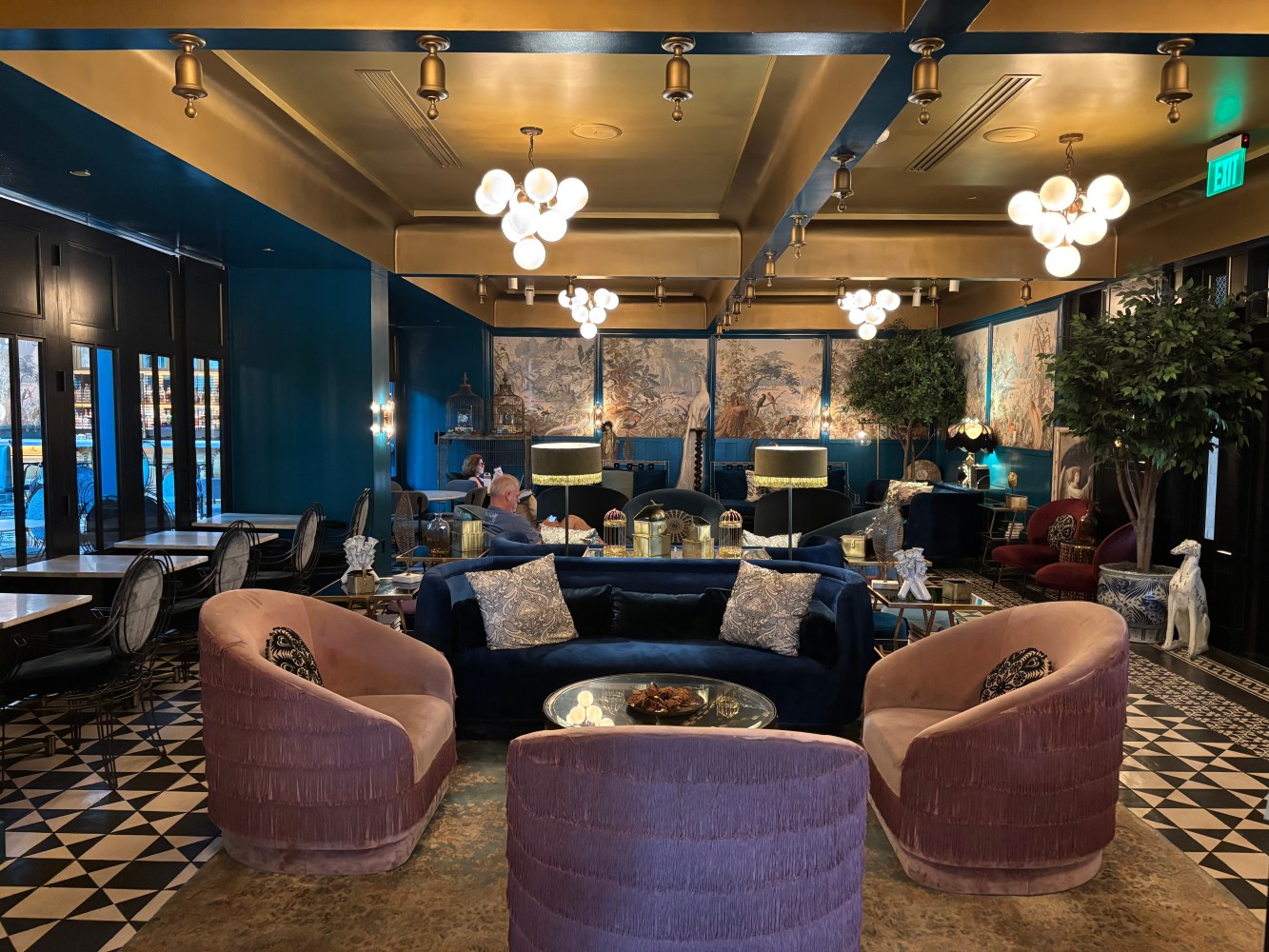 Luxury lounge with velvet seating, chandeliers, and decorative wallpaper.