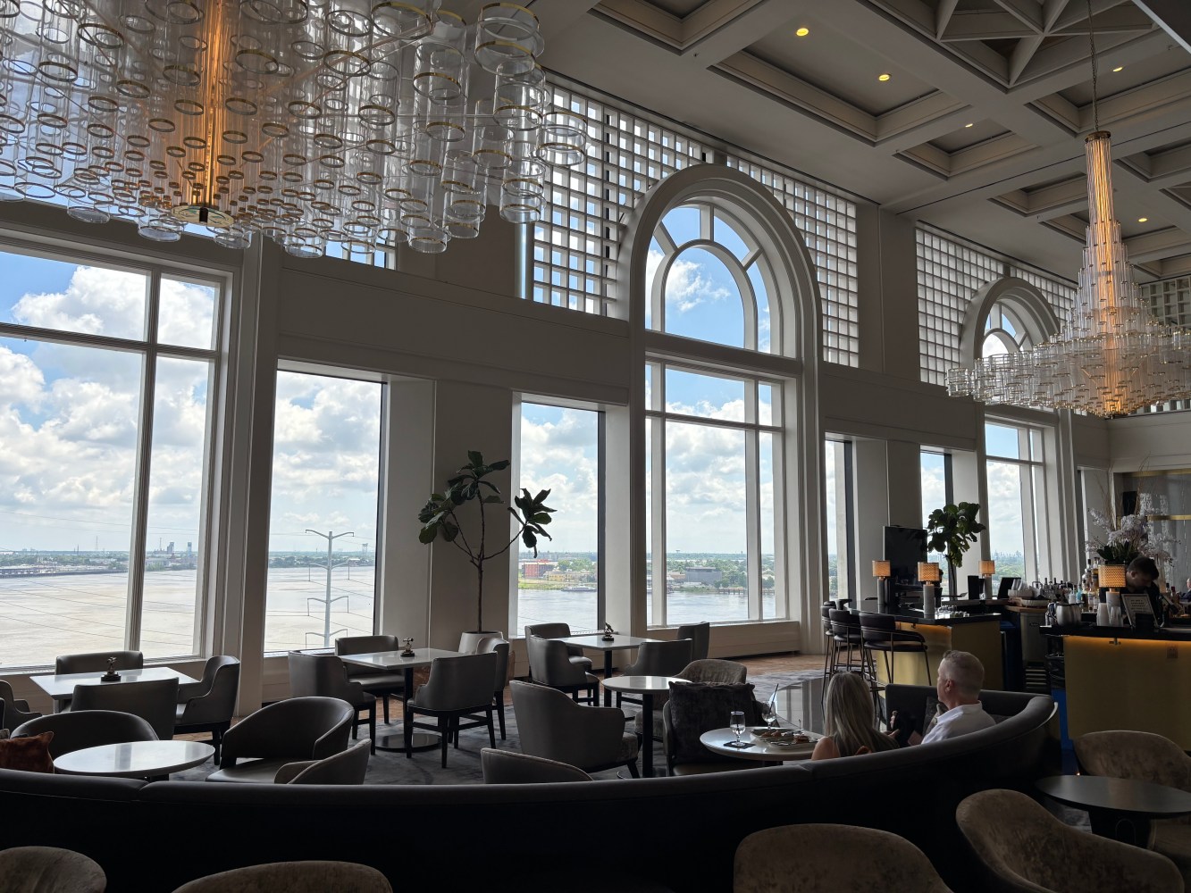 Elegant lounge with large arched windows and chandeliers overlooking an airport runway.
